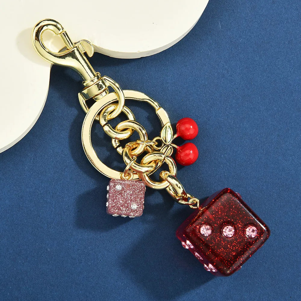 Close-up of a cherry red and white metal dice keychain pendant with a square pattern on a vintage-style suitcase charm.