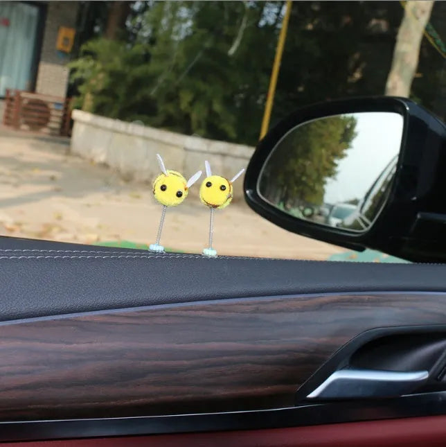 Small yellow and black fur ball bee car decoration on a plastic surface.