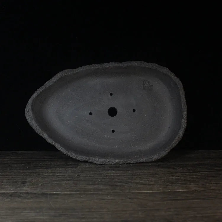 Handmade purple clay flower pot with creative shape on floor next to plant.
