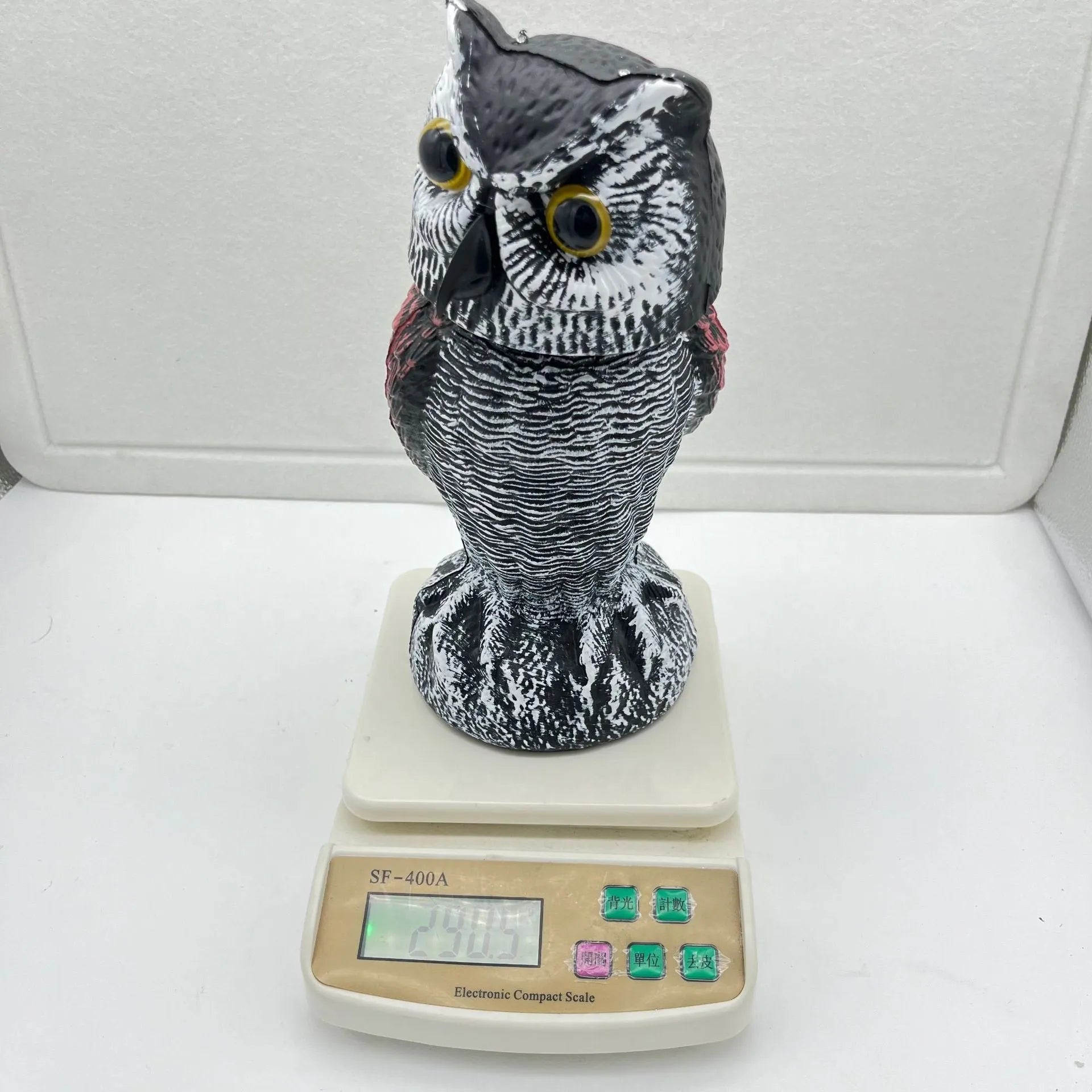 A detailed artificial owl bird scare ornament with a shaking head, shown in a garden setting.
