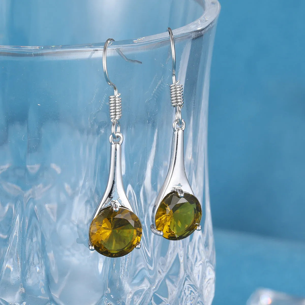 Olive green topaz coloured water drop shape earrings with minimalist retro styling on white background