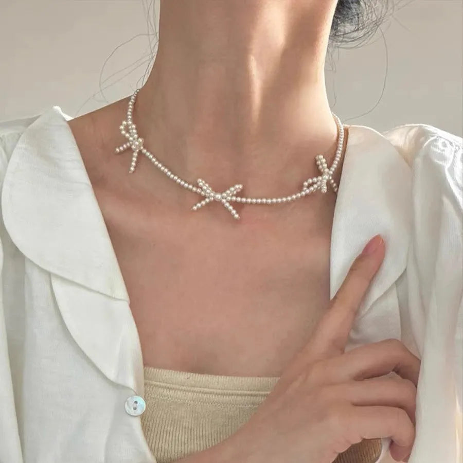 White geometric bow detail on an adjustable imitation pearl necklace for women, chain length 31-40cm.